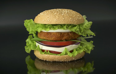 Tasty burger on black background. Homemade hamburger with fresh vegetables.