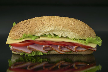 fresh submarine sandwich with ham, cheese, bacon, tomatoes, lettuce on dark background