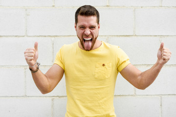 Funny young man on brick wall with funny expression sticking out tongue.