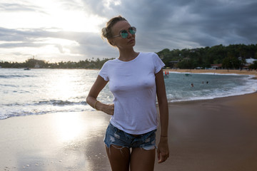 Fototapeta na wymiar Beautiful young woman in a white t-shirt on the beach. Mock-up.