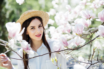 Young beauty woman in straw hat around magnolia pink flowers tree in spring garden