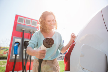 A woman stands at the charging station and holds a plug of the charger for an electric car