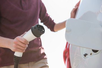 A man stands at the charging station and holds a plug of the charger for an electric car