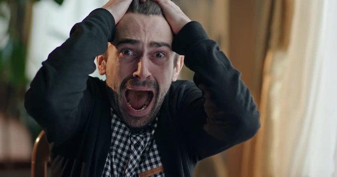 Distraught man reacting with grief while sitting on chair at home