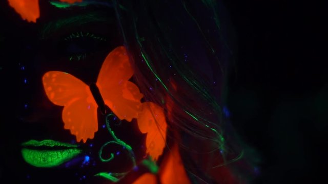 Shooting close-up of a girl with green lips and an orange butterfly on her cheek