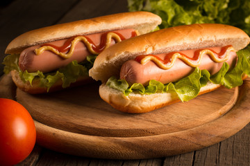 Photo of barbecue grilled hot dog with yellow mustard and ketchup on wooden background. Hot dog sandwich with potato fries and sauces.