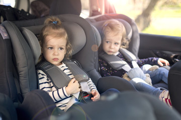 cute small twins in car seats in the car