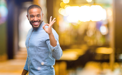 African american man with beard doing ok sign with hand, approve gesture at night