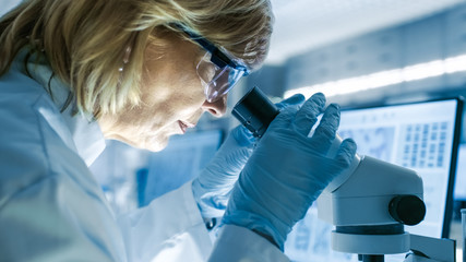 Senior Female Biologist Works on Her Computer and Looks at Materials under Microscope. She's in a...