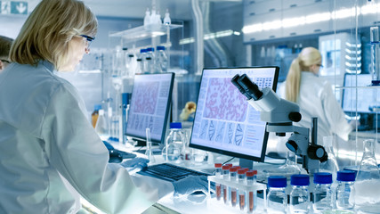 Senior Female Scientist Works with High Tech Equipment in a Modern Laboratory. Her Colleagues are...