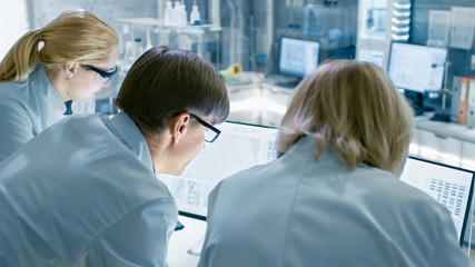 Back View of Team of Senior and Young Scientists Working on Problem Solution. They're Looking for...