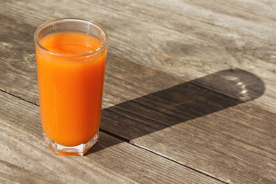 Carrot or orange fresh juice on wooden table outdoors with sunlight