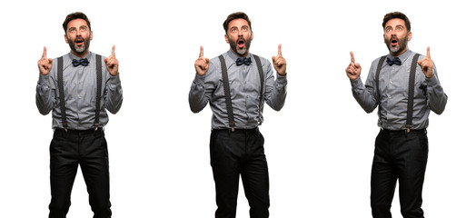 Obraz premium Middle age man, with beard and bow tie happy and surprised cheering expressing wow gesture pointing up