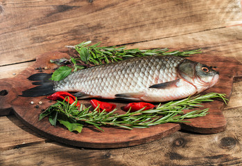 Fresh fish with herbs and pepper before cooking on wooden background