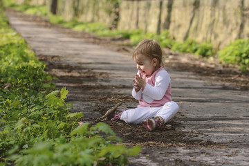Happy little baby playing while sitting on the road in the park.