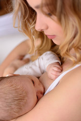 Obraz na płótnie Canvas Breastfeeding baby close up. Pretty mother holding her newborn child. Mom nursing baby. Beautiful woman and new born relax at home. Blondе mother breast feeding baby.