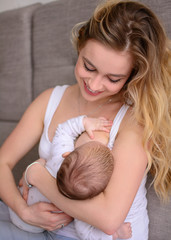 Obraz na płótnie Canvas Breastfeeding baby. Pretty mother holding her newborn child. Mom smile and nursing infant. Beautiful woman and new born love at home. Blondе mother breast feeding baby.