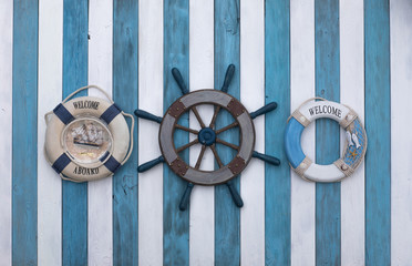 old wooden ship's steering wheel and lifebuoy on a blue white wooden background