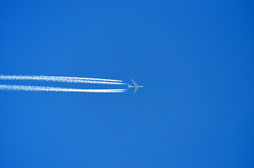 Airplane flying high above in the blue sky, leaving contrail behind