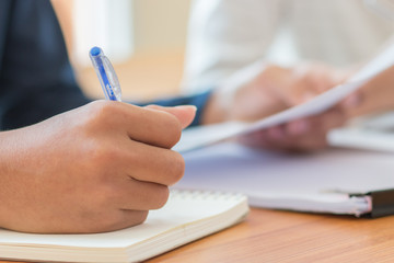 Students holding pen in hands taking exams, writing examination room with undergraduate students inside. Student sitting learning lessons on row desk chair doing final exam in classroom with uniform.