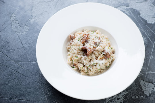 Risotto with chanterelles and parmesan cheese served in a white plate on a grey concrete background