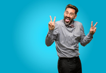 Fototapeta premium Middle age man, with beard and bow tie looking at camera showing tong and making victory sign with fingers