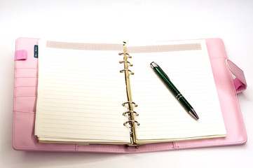 pink notebook with a ballpoint pen lying on white background