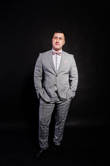 Fototapeta premium Studio portrait of man in gray suit and bow tie against black background.