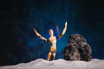 Conceptual picture of a burning wooden figure of a man standing on his knees with his hands up in front of a stone in a deserted landscape. The symbol of despair and appeals to the "higher forces"