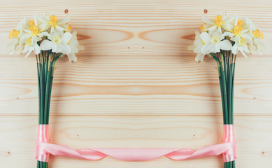 frame of bouquets of daffodils flowers tied with pink ribbon on a natural wooden background with copy space for text