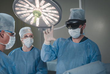 Group of surgeons using augmented reality holographic hololens glasses while operating in modern...
