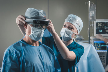 Nurse assisting surgeon with mounting augmented reality holographic hololens glasses before...