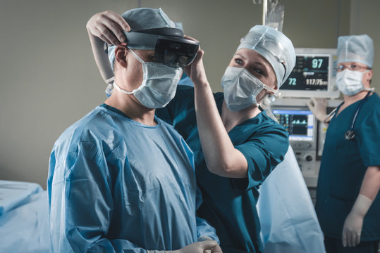 Nurse assisting surgeon with mounting augmented reality holographic hololens glasses before operation
