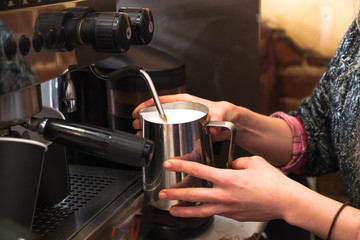Barista preparing milk for takeaway coffee. Close-up view on hands, small coffee business concept.