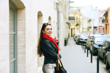 Fototapeta premium Portrait of a young beautiful woman, girl posing on the streets of a European city . The model is dressed in a stylish leather jacket