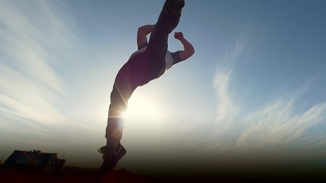 Young male Parkour tricker jumper performs amazing flips in front of the sun