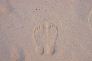 White sand beach with bare foot marks in sunrise light. Sand beach top view.