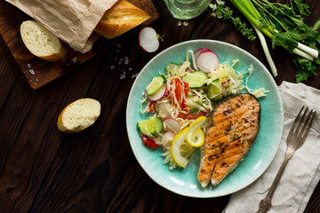 Grilled salmon steak and vegetarian vegetable salad of radish, cucumbers, lettuce salad. Healthy proper nutrition. Copy space, top view flat lay background.