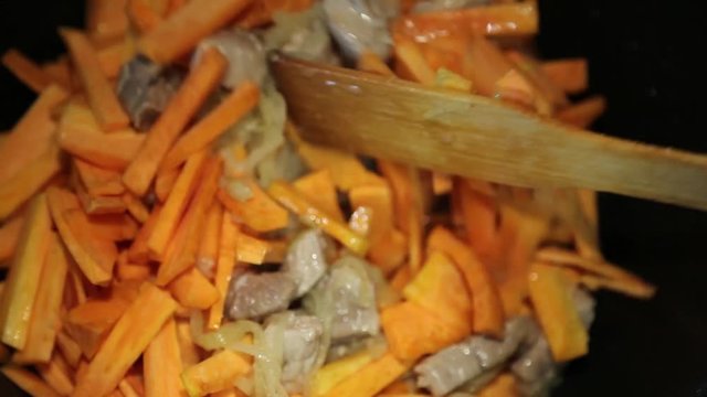 Preparation of rice dishes - pilaf from Uzbekistan. In a saucepan with onions and meat, chopped carrots are added for roasting.