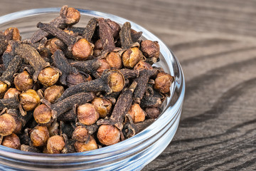 Close-up of spicy dried cloves in glass. Syzygium aromaticum. Decorative bowl with the pile of aromatic medicinal spices with distinctive scent on wood background. Great depth of field.