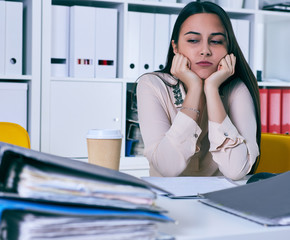 Tired and exhausted woman looks at the mountain of documents propping up her head with her hands.
