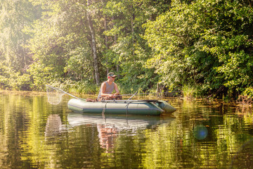 Fisherman with fishing rods is fishing in a rubber boat against background of beautiful nature and lake or river. Camping tourism relax trip active lifestyle adventure concept