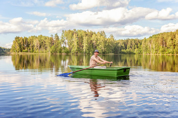 Fototapeta na wymiar Fisherman with fishing rods is fishing in a wooden boat against background of beautiful nature and lake or river. Camping tourism relax trip active lifestyle adventure concept