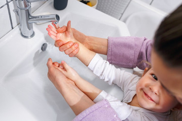 Fototapeta premium Happy mother and smiling kid girl wash hands with soap in bathroom top view.