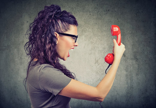 Woman holding red telephone receiver and yelling in anger.