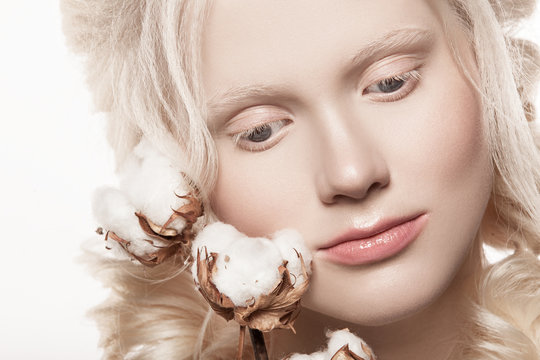  A beautiful albino girl photographed on a white background in the studio. Natural color of the lips and hair pigtail. The girl is holding soft cotton flowers.