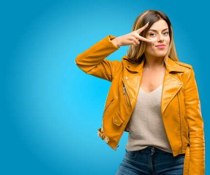 Beautiful young woman looking at camera through her fingers, blue background