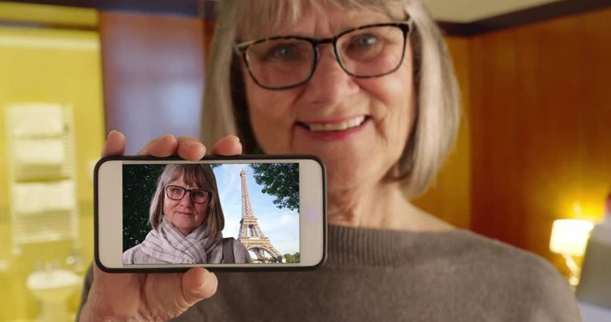 Sweet old woman showing picture of herself in Paris by Eiffel Tower to camera, Mature white female showing smartphone picture of herself from her vacation in Paris, France, 4k