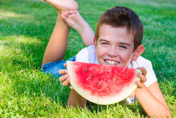 Child eating juicy watermelon outdoors on grass