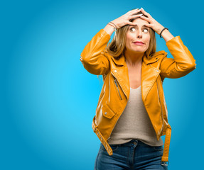 Beautiful young woman stressful keeping hands on head, terrified in panic, shouting, blue background